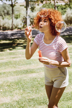 Beautiful young woman blowing bubbles in a park