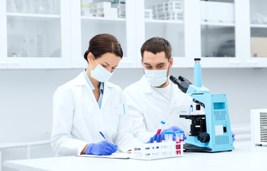 scientists with clipboard and microscope in lab