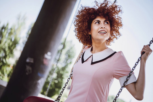 Trendy Young woman playing like a little girl on swings in a par