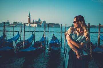 Beautiful well-dressed woman standing near San Marco square with gondolas and Santa Lucia island on...