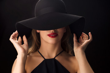 beautiful woman in black hat over dark background