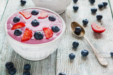Breakfast bowl with yougurt, muesli, fresh blueberries and strawberries. Light wooden background