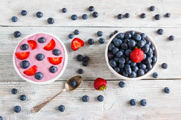 Naklejka na ściany i meble Breakfast bowl with yougurt, muesli, fresh blueberries and strawberries. Light wooden background, top view.