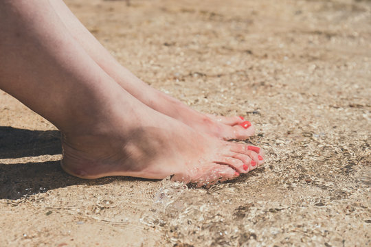 female feet with red pedicure in beach sand, close up