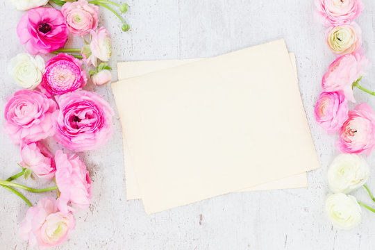 Pink and white ranunculus flowers with aged blank paper note on white wooden background flat lay scene
