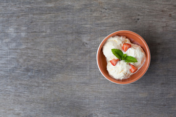 Dairy ice cream topped with mint and strawberries in the bowl on a dark wooden table, selective focus