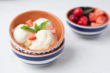Dairy ice cream topped with mint and strawberries in the bowl on a  white table, selective focus