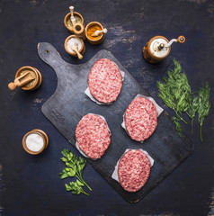 concept of home cooking chops of marble beeffour cutlets are laid out on vintage cutting board on a blue rustic wooden background with parsley and dill and spices,  top view
