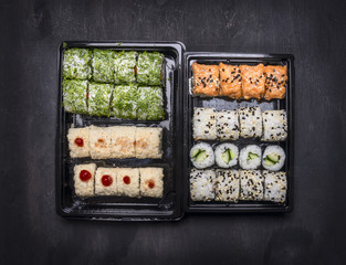 Japanese fast food, sushi set with two variousingredients in plastic containers on a dark rustic background, top view