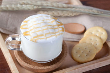 close up hot milk and caramel on top with biscuits on wooden pla
