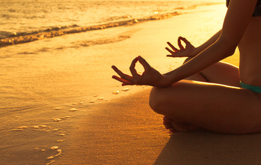 hand of a woman meditating in a yoga pose on the beach at sunset

