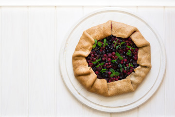 Homemade galette pie with red and black currants, blueberries and raspberries on wooden background. Top view