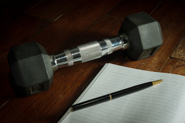 Metal dumbbell with book and pen.