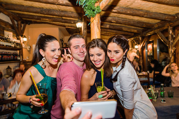 Young beautiful people with cocktails in bar taking selfie