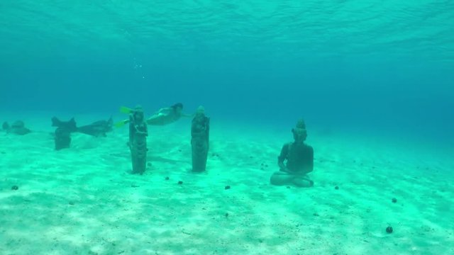 Woman diving underwater exploring sunken statues on the sea bottom