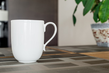 Morning white cup of coffee or tea on a wooden kitchen table with a plant on a background. Dark brown colors. Focus at handle