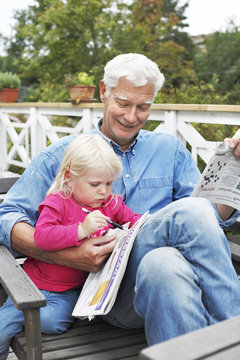 Sweden, Bohuslan, Senior man sitting with girl (2-3) doing crossword puzzle