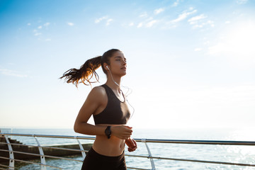 Picture of young attractive fitness girl jogging with sea on background - obrazy, fototapety, plakaty