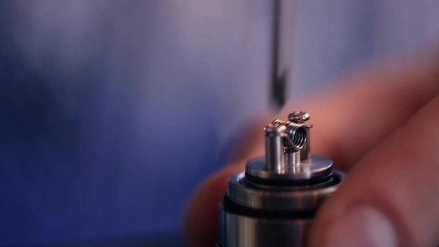 Hand with a screwdriver, unscrews screws holding wire heating element in electronic cigarette.