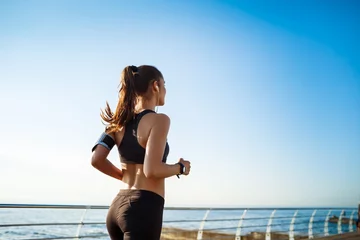 Fotobehang Foto van jonge aantrekkelijke fitness meisje joggen met zee op background © Cookie Studio