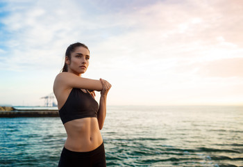 Picture of young beautiful fitness girl makes sport exercises with sea on background