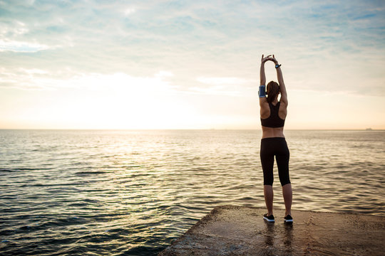 Picture of young beautiful fitness girl makes sport exercises with sea on background