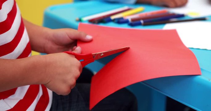 Cute little boy cutting paper shapes classroom