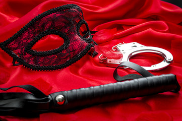 Concept image with a mask, hand cuffs and a flogger covered in rose petals on red silk. BDSM is a variety of erotic practices or role playing involving bondage, dominance and submission, masochism © Victor Moussa