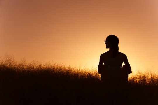 Young woman sitting in a field watching the sunset.

