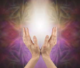 Pranic healer sensing energy  -   female hands reaching up into a soft white light with a gold pink and purple energy formation behind and copy space 