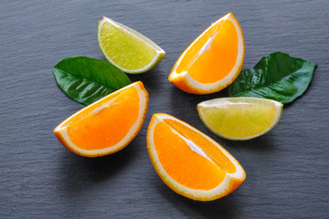 Orange and lime sliced segments with green leaves on black slate stone. Vitamin concept