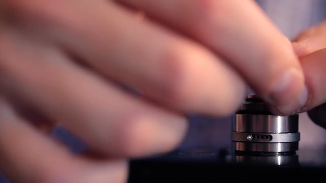Installation by hands winding metal spiral at base, electronic cigarette closeup.