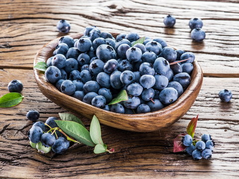 Ripe blueberries in the bowl on the wooden table.