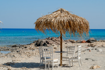 white chairs and table with view of tropical turquoise ocean under a straw umbrella