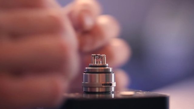 Dismantled electronic cigarette to replace wick hands closeup.