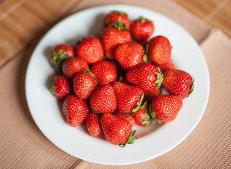 bright, ripe, delicious strawberries in a white plate on a wooden background