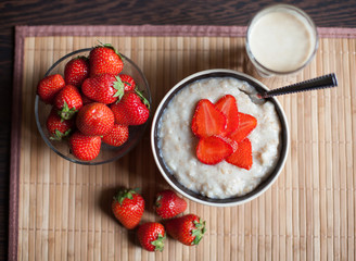 hot oatmeal, with pieces of strawberries and warm cocoa with milk on a wooden table