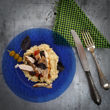 Traditional italian risotto with chicken, tomato, basil and parmesan on blue plate with knife and fork and glass of wine