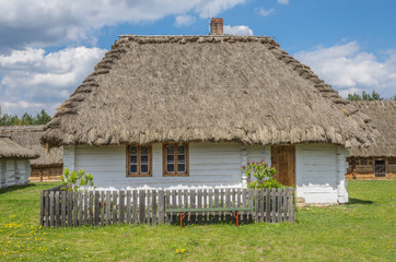 wiejski mały, biały domek pokryty strzechą z ogródkiem
