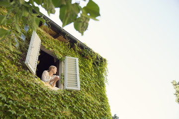 Woman looking out from window overgrown house