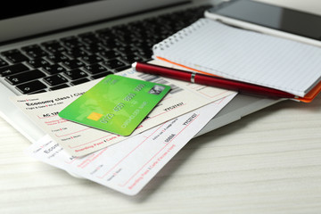 Laptop with mobile phone, credit card and flight tickets on light wooden table