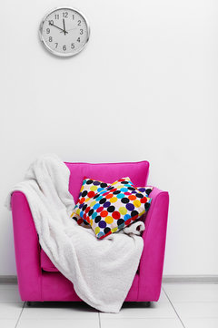 Pink armchair with blanket and pillows on light wall background