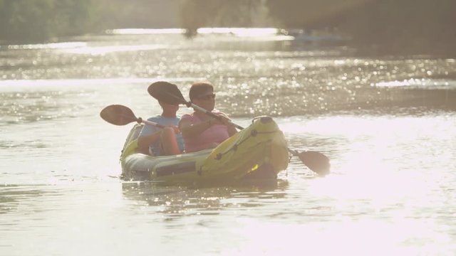 SLOW MOTION: Smiling mature couple canoeing at golden summer sunset