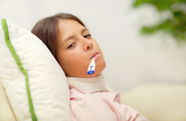 Cold girl lying on the couch with a thermometer in her mouth
