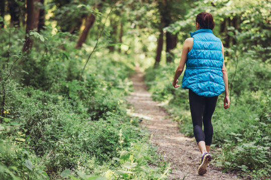 Walking young sporty woman in blue warm sleeveless jacket on the nature, park, forest background. Sport.