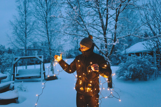 Finland, Jyvaskyla, Saakoski, Young man holding Christmas lights in backyard at dusk