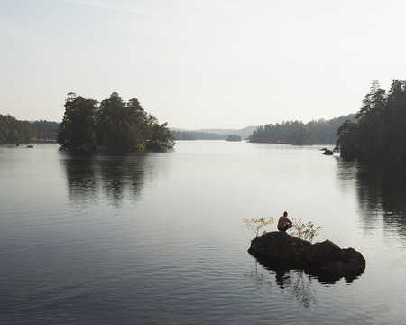 Sweden, Blekinge, Man crouching on rock on Lake Halen