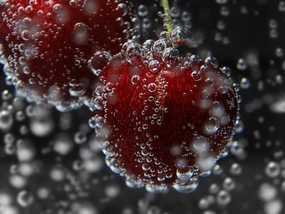 Cherry in water with bubbles close up on dark background