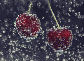 Cherry in water with bubbles close up on dark background
