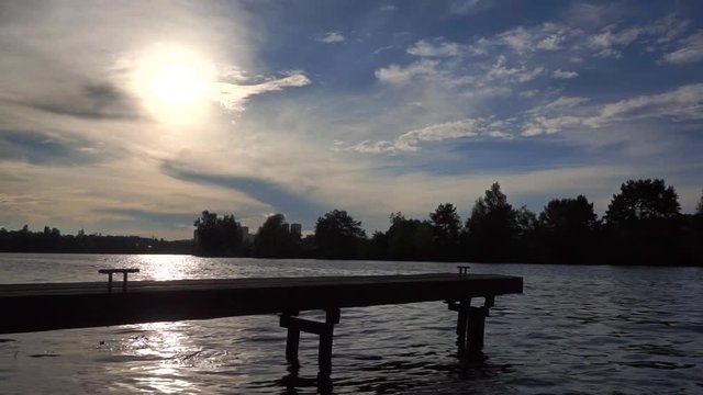 Silhouette of small river pier against evening sun. Wide shot, slow motion